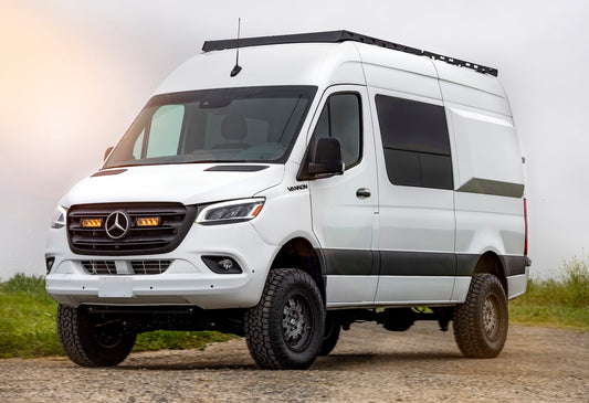 A white Mercedes-Benz Sprinter van with black fenders and off-road tires, parked outdoors.