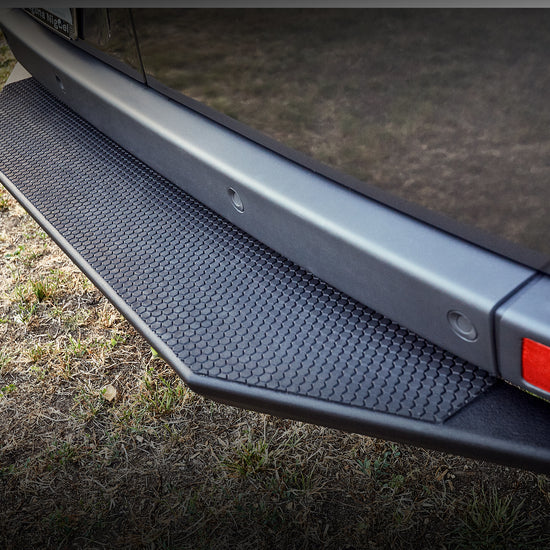 Black aluminum rear entry step with a crinkle black powder-coated finish attached to the rear bumper of a vehicle.