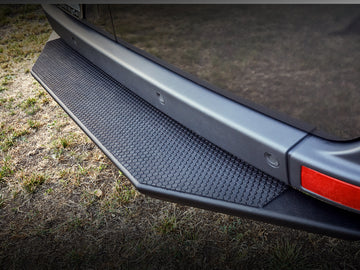Black aluminum rear entry step with a crinkle black powder-coated finish attached to the rear bumper of a vehicle.