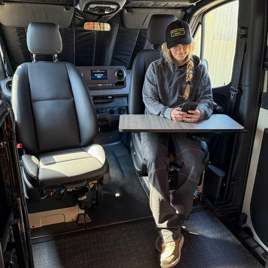 A person seated in a Sprinter van cabin, using a mobile device, with a空 table mounted on the side of the van interior