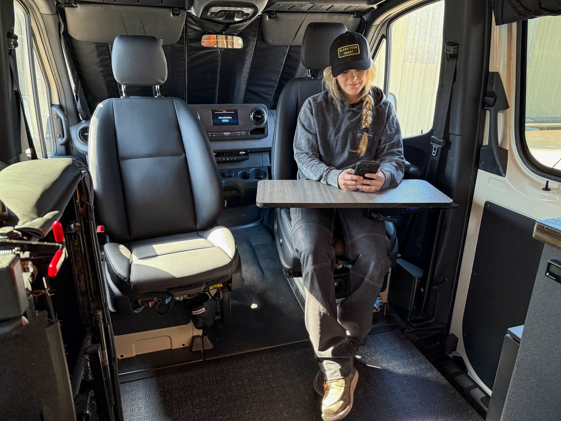 A person seated in a Sprinter van cabin, using a mobile device, with a空 table mounted on the side of the van interior