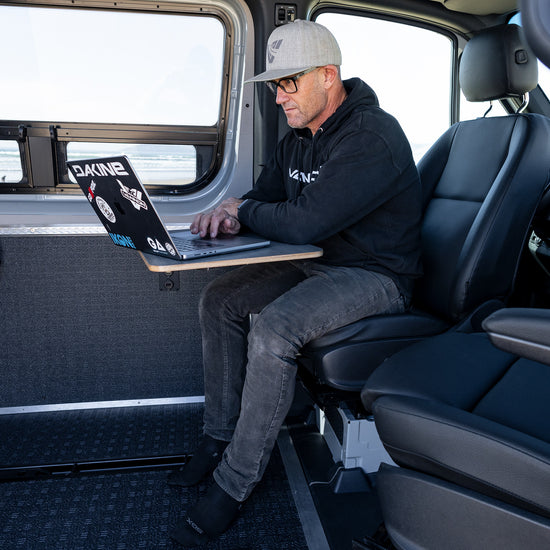 A person seated in a Sprinter van with a laptop on their lap, showcasing the interior and potential use of the VANNON Lagun B-Pillar Mount.