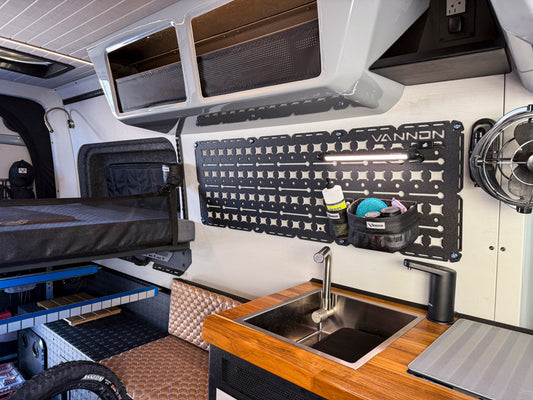 A black nylon storage panel named 'Walle' mounted on a wall inside a vehicle, equipped with various straps and hooks for organizing gear.