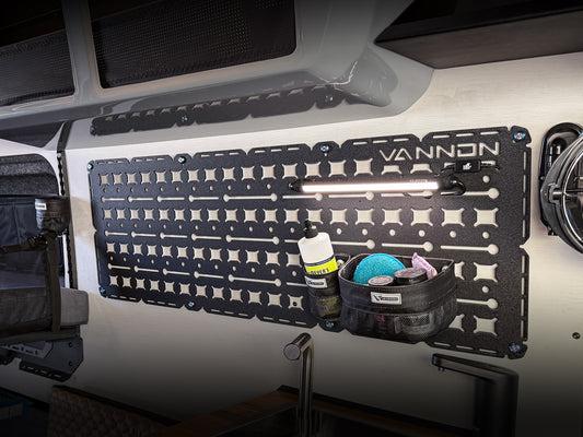 A black nylon 'VANNON Walle Panel' mounted on the wall inside a vehicle, featuring a grid of storage compartments with various items organized within.