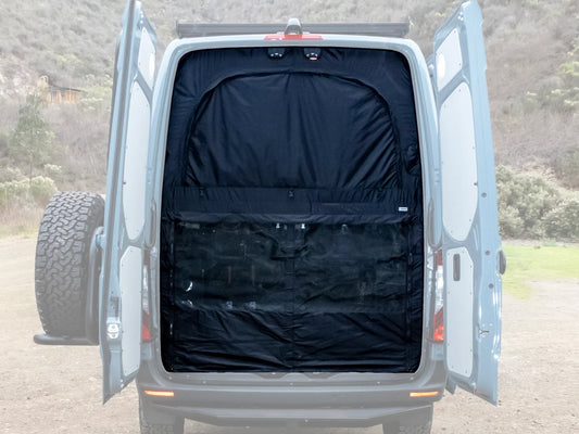 A black VANNON Storm Wall installed on the rear door of a white van, appearing as a mesh screen with a solid black panel on the inside.