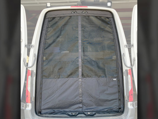 A black rear bug screen installed on the rear window of a white van, made of nylon mesh with a magnetic closure.