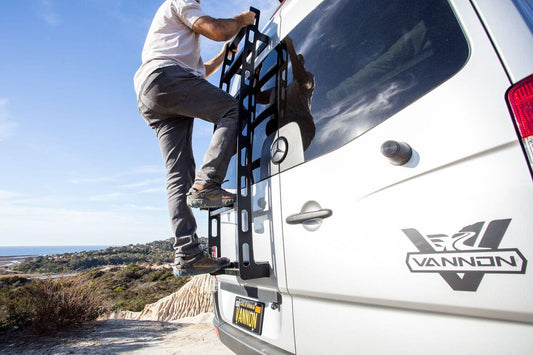 Man climbing ladder on the back of a VANNON adventure van.